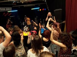 Veranstaltung im Safe-Jugendclub. Eine Gruppe Jugendlicher steht vor einer Bühne im Clubraum. Auf der Bühne spielt eine Musikgruppe. Beispielbild für Jugendtreffs in Kamenz.