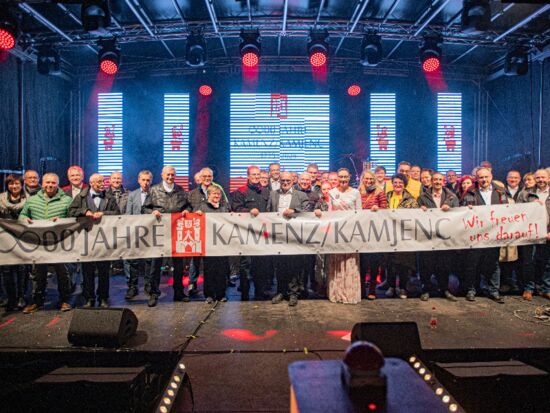 Mehrere Personen halten auf der Bühne stehend ein Banner in der Hand mit der Aufschrift 800 Jahre Kamenz