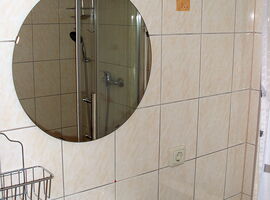 Ein Waschbecken mit rundem Spiegel und Beleuchtung im Badezimmer der Ferienwohnung Voigt. Rechts daneben ein Fenster.. 