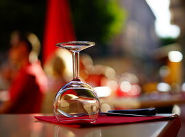 Weinglas umgedreht auf einem gedeckten Tisch mit Serviette und Besteck. Im Hintergrund verschwommen weitere Tische und Restaurant-Gäste. Beispielbild / Stimmungsbild für Kulinarik in Kamenz.. 