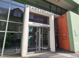 Außenansicht des Stadttheater Kamenz. Glasfront im Eingangsbereich mit Tür und der Aufschrift Stadttheater Kamenz und sorbischer Bezeichnung.
