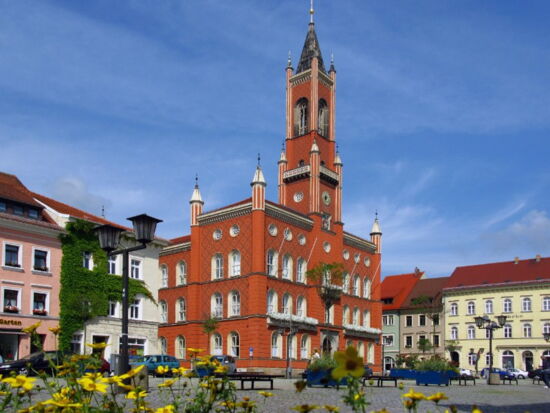 Marktplatz in Kamenz mit Rathaus im Zentrum und Wohn- und Geschäftshäusern drumherum. Aufnahme bei Sonnenschein mit Blumenschmuck im Vordergrund. Beispiel für Sehenswürdigkeiten in Kamenz.