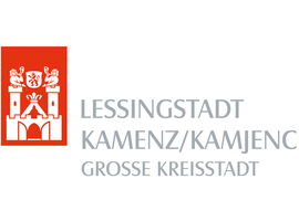 Logo der Lessingstadt Kamenz in den Kamenz-Farben rot und grau. Ein Wappen mit zwei Türmern auf der Stadtmauer und der Beschriftung Lessingstadt Kamenz /Kamjenc Große Kreisstadt daneben.. 