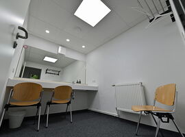 Beispielansicht des Backstage-Bereiches der Hutbergbühne Kamenz. Ein Garderobenraum mit einem Wandspiegel, Tisch / Schminktisch und Stühlen.. 