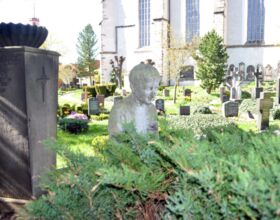 Steinfigur und verschiedene Gräber des Friedhofes, welcher um die Kirche herum liegt