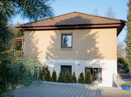 Außenansicht der Ferienwohnung Kurtzke. Ein zweistöckiges Haus mit gepflasterten Platz und Hecke davor.. 