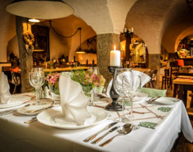 Einblick in den Gastronomieraum Ratskeller im Hotel Goldner Hirsch. Ein eingedeckter Tisch im Vordergrund mit Geschirr, Besteck, einer Kerze und Servietten. Im Hintergrund weitere Tische. Beispiel für Gastronomie in Kamenz.