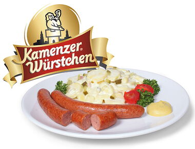 Ein Teller mit zwei Kamenzer Würstchen darauf sowie Kartoffelsalat und Senf. Im Vordergrund das Logo der Kamenzer Würstchen - ein Emblem mit Stadtschreier Logo und Schriftzug. Beispiel für Kulinarik und Werbekampagnen in Kamenz.. 