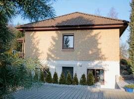 Außenansicht der Ferienwohnung Kurtzke. Ein zweistöckiges Haus mit gepflasterten Platz und Hecke davor.