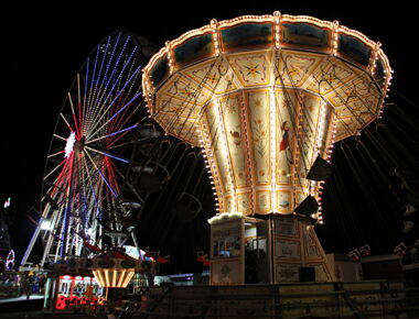 Rummelbetrieb auf dem Kamenzer Forstfest bei Nacht. Ein erleuchtetes Kettenkarussel dreht sich im Vordergrund. Im Hintergrund ein Riesenrad und kleinere Fahrgeschäfte. Beispiel für Veranstaltungen in Kamenz.