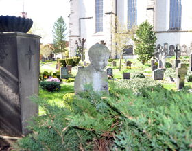 Steinfigur und verschiedene Gräber des Friedhofes, welcher um die Kirche herum liegt. 