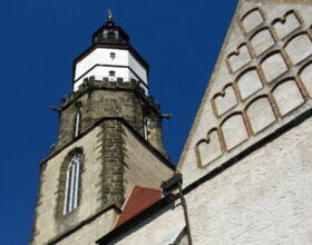 Blick von unten auf den Turm der Hauptkirche St. Marien mit blauem Himmel