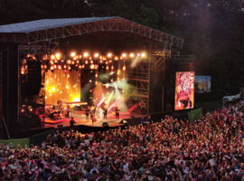 Hutbergbühne mit Beleuchtung und Musikern beim Konzert. Rechts an der Bühne eine digitale Leinwand. Im Vordergrund steht das feiernde Publikum. Beispiel für Bühnen in Kamenz.
