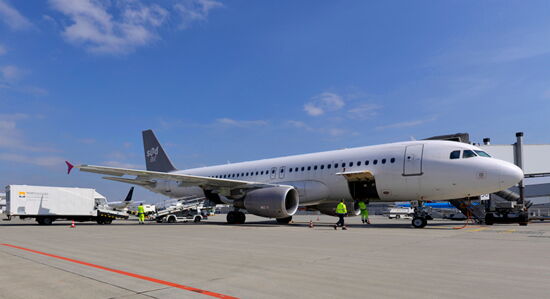 Ein Flugzeug auf dem Flughafen in Dresden während der Abfertigung. Verschiedene Arbeiter bereiten das Flugzeug für die nächste Reise vor und arbeiten am Flugzeug. Im Hintergrund Lastwagen und weitere Flugzeuge.