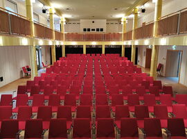 Einblick in den Theatersaal des Stadttheater Kamenz. Reihen mit roten Stühlen sind hintereinander aufgebaut. Oben ist eine weitere Etage mit Sitzülätzen und der Regieraum. Beispiel für Innenansicht des Kamenzer Stadttheaters.. 