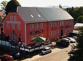 Außenansicht des Goldnes Band Gersdorf. Ein großer Gasthof an der Hauptstraße in Haselbachtal. Auf der offenen Terrasse des Eiscafés sitzen zahlreiche Besucher. Davor parkende Autos.. 
