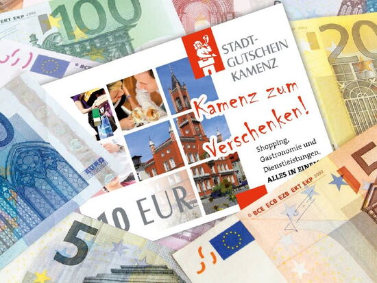 Ansicht des Kamenzer Stadtgutscheins inmitten von Geldscheinen. Beispielbild der Stadtgutschein Wertkarte, die als passendes Geschenk für jede Gelenheit gekauft und bei allen teilnehmenden Akzeptanzstellen in Kamenz eingelöst werden kann.. 