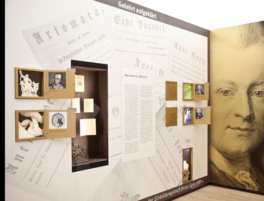 Innenansicht der Ausstellung im Lessing-Museum. Ausstellungsteil "Gelehrt aufgeklärt" mit ausgestellten theoretischen Schriften, einer kleinen griechischen / römischen Laokoon-Skulptur und Bild- und Hinweistafeln. Rechts ein großes Bild von Lessing.. 