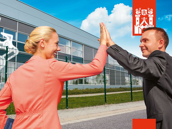 Kampagnen-Bild der Stadtkampagne Neue Stadt. Neues Glück zum Thema Arbeiten. Ein Mann und eine Frau in Businesskleidung stehen vor einer Arbeitsstätte und klatschen einander auf die erhobene Hand.. 