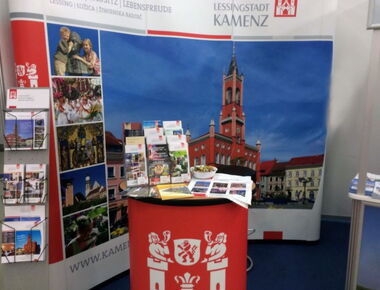 Messestand der Stadt Kamenz bei Tourismusmesse. Beispiel für Messen und Präsenationen des Stadtmarketing. Ein Stand mit Präsentationswand und Bildern von Kamenz, Broschürenaufstellern, Messetisch und Postkarten und Kamenz-Tüten.. 