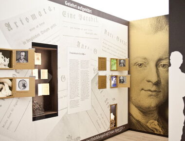 Innenansicht der Ausstellung im Lessing-Museum. Ausstellungsteil "Gelehrt aufgeklärt" mit ausgestellten theoretischen Schriften, einer kleinen griechischen / römischen Laokoon-Skulptur und Bild- und Hinweistafeln. Rechts ein großes Bild von Lessing.. 