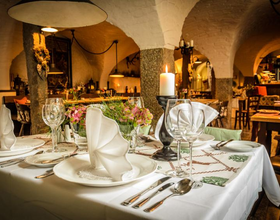 Einblick in den Gastronomieraum Ratskeller im Hotel Goldner Hirsch. Ein eingedeckter Tisch im Vordergrund mit Geschirr, Besteck, einer Kerze und Servietten. Im Hintergrund weitere Tische. Beispiel für Gastronomie in Kamenz.. 