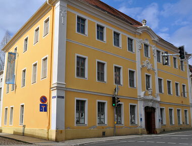 Außenansicht des Museums der Westlausitz - Elementarium. Das Museum befindet sich im Ponickauhaus - einem gelben dreistöckigen Gebäude mit weißen Stuckelementen an der Front. An der linken Wand ein Banner mit der Aufschrift Elementarium.. 