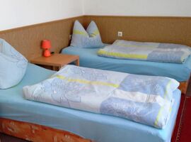 Schlafzimmer Beispiel mit zwei Einzelbetten und Blumenbettwäsche. Dazwischens teht ein hölzerner Beistelltisch mit Leuchte. An der Wand sind eine Holzverkleidung und weiße Tapete.