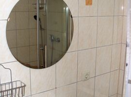 Ein Waschbecken mit rundem Spiegel und Beleuchtung im Badezimmer der Ferienwohnung Voigt. Rechts daneben ein Fenster.