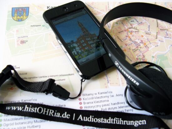 Ansicht des Kamenzer Multimediaguides. Ein schwarzer I-Pod mit Kopfhörern, um selbständig eine Stadtführung durchführen zu können. Im Hintergrund der dazugehörige Stadtplan.